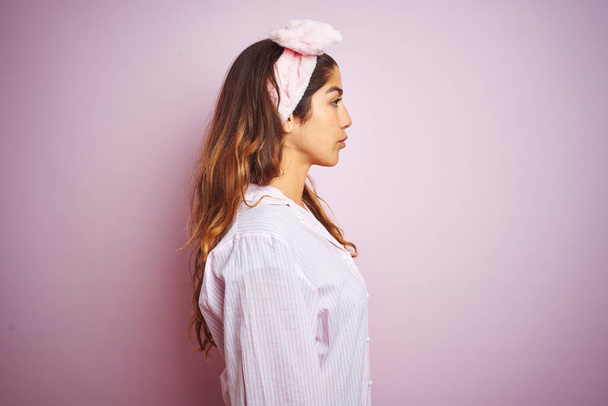 Fiatal gyönyörű nő visel pizsama felett álló rózsaszín elszigetelt háttér keres oldalra, pihenjen profil pózol természetes arc magabiztos mosollyal. - Fotó, kép