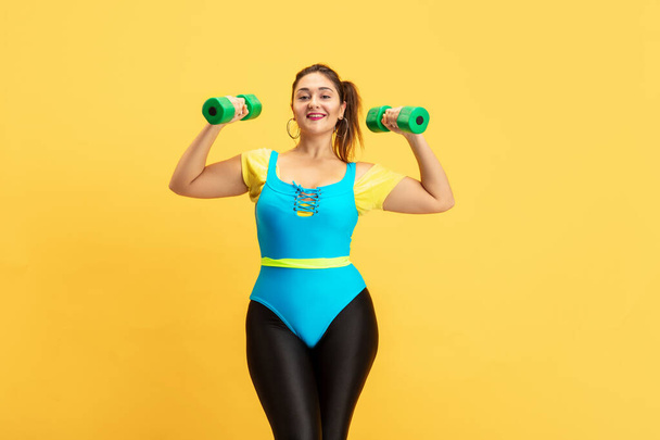 Young caucasian plus size female models training on yellow background - Foto, afbeelding