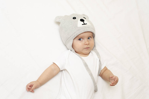 Infant baby in grey teddy bear hat on a white background. Concept of winter, hug, cozy, hygge. - Photo, Image