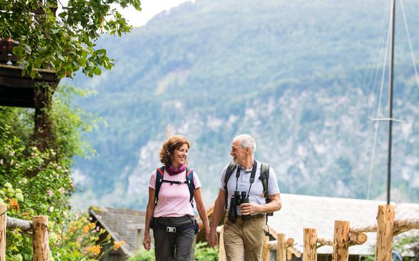A senior pensioner couple with binoculars hiking, walking. - Foto, Bild
