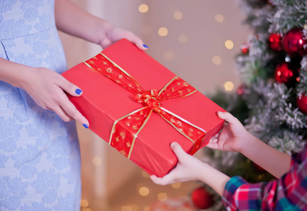 Woman give a child Christmas red gift box with Christmas tree on the background - Фото, зображення