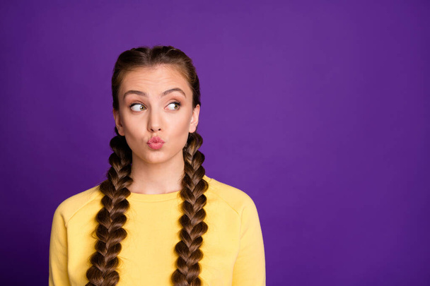 Photo of funny expression lady with long braids hairdo sending air kisses looking cunning empty space wear casual yellow pullover isolated purple color background - Photo, image