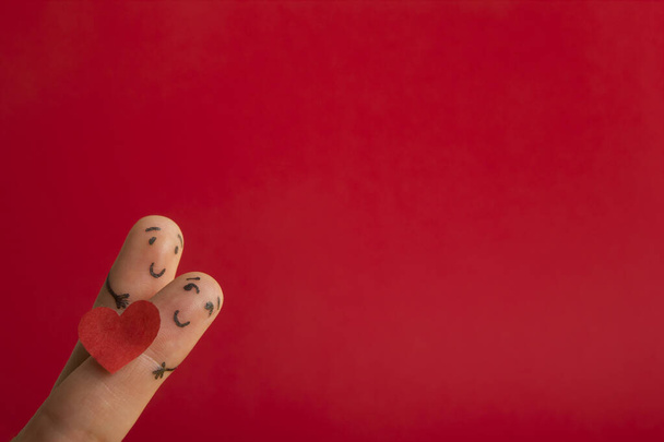 Valentýn se zamiluje do konceptu. Malované šťastné prsty smajlík v lásce s červeným srdcem proti červenému pozadí - Fotografie, Obrázek