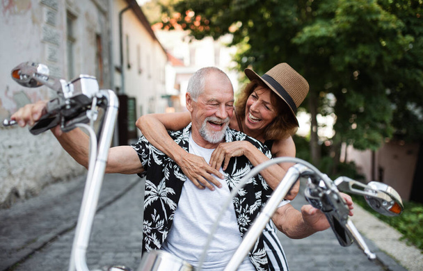 A cheerful senior couple travellers with motorbike in town. - Foto, afbeelding