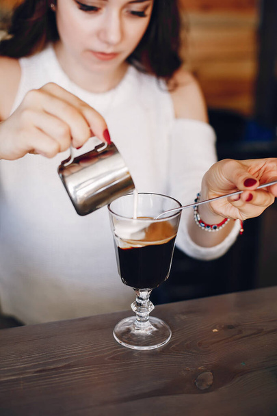 Woman in a white sweater pouring milk into coffee dessert - Foto, Imagem
