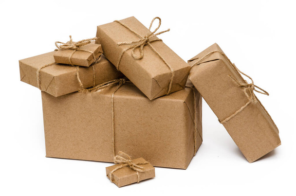 Куча упакованных коробок, обернутых коричневой крафтовой бумагой и завязанных бечевкой на белом фоне. Крупный план. Концепция доставки, перемещения, упаковки и подарков
 - Фото, изображение