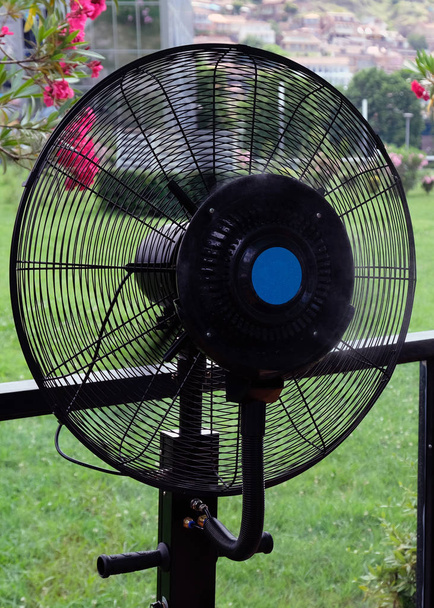 Černý větrák s zvlhčovačem v kavárně za horkého letního dne. Speciální ventilátor s vodní tříští pro chlazení v horku. - Fotografie, Obrázek