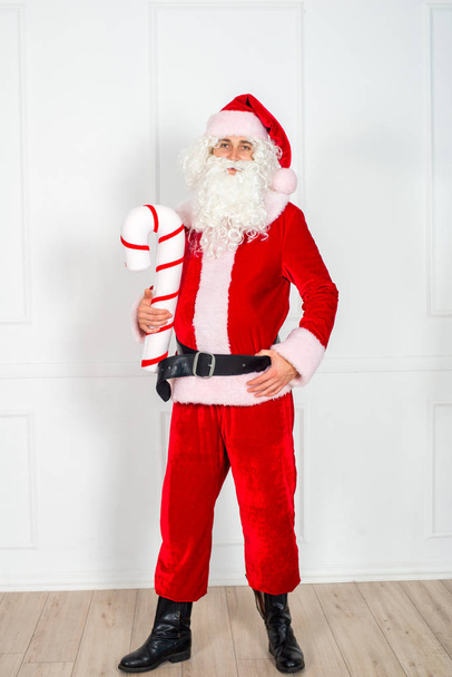 Święty Mikołaj w klasycznym czerwonym garniturze z białą brodą na białym tle w studio. Wspaniali noworoczni bohaterowie. Świąteczny nastrój. - Zdjęcie, obraz