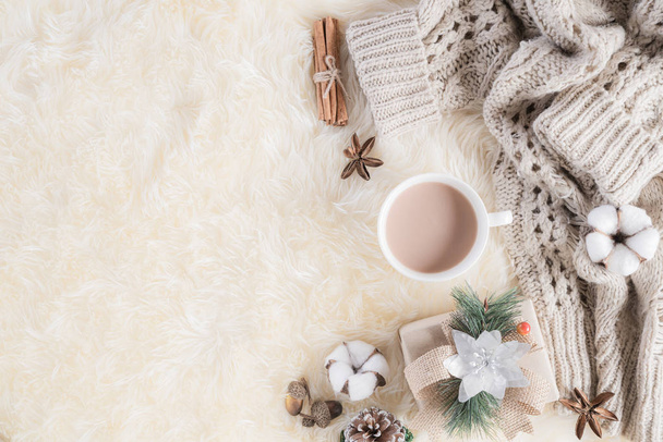 Autumn or winter composition. Gift box Coffee cup, cinnamon sticks, anise stars, beige sweater with knitted blanket on cream color gray fluffy background. Flat lay top view copy space. - Photo, Image