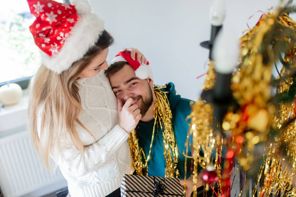 νεαρό ζευγάρι με χριστουγεννιάτικα καπέλα διακοσμεί το σπίτι για τα Χριστούγεννα - Φωτογραφία, εικόνα