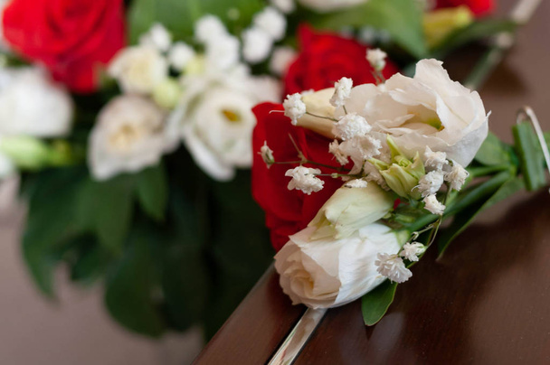 soft focus of groom boutonniere with red and white flowers in front of bridal bouquet with roses on couch at home - Фото, зображення