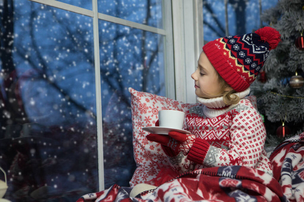 Kleines Mädchen sitzt am Fenster und am Weihnachtsbaum - Foto, Bild