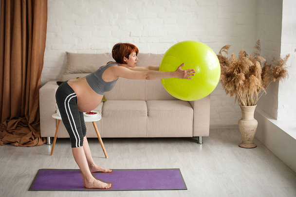 Egy gyönyörű fiatal terhes nő portréja. Edzések fitball otthon. - Fotó, kép