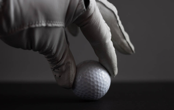hand in glove keep golf ball on black background - Foto, imagen