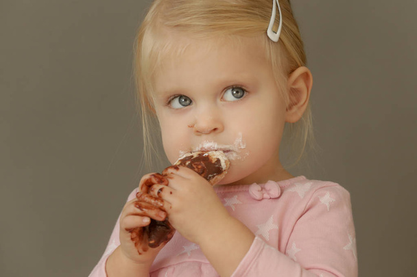 Studio shot of two years old girl eating cone ice cream. Sugar and sweets addiction concept among children.  - Photo, Image