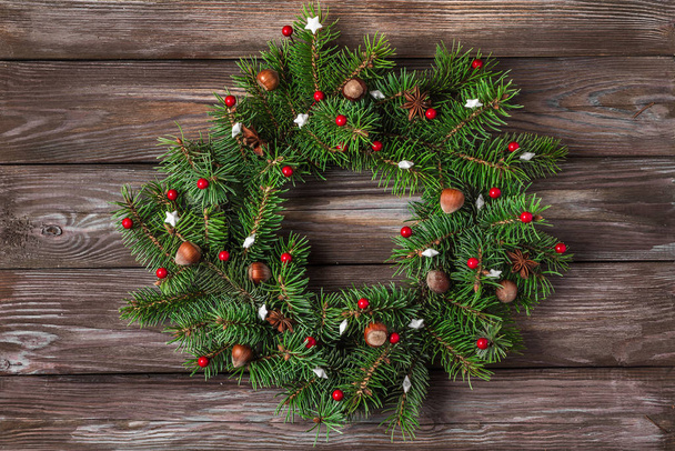 Christmas wreath made of fir tree branches, red decorations, nuts, pine cones on rustic wooden background - Photo, Image