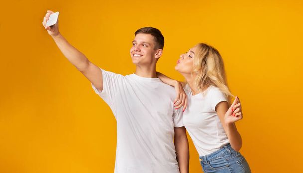alegre millennial pareja tomando selfie, de pie sobre amarillo fondo
 - Foto, imagen