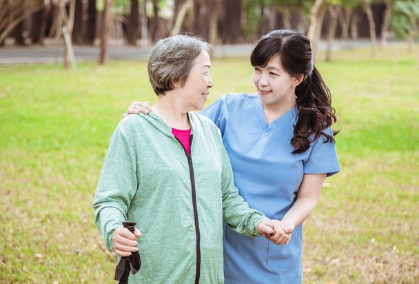 Smiling nurse helping senior woman to walk around the park - Photo, Image