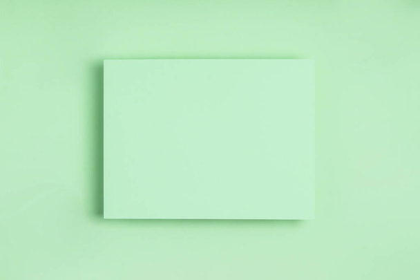 Minimal frame geometric composition mock up. Blank sheet of delicate green paper on green background. Template design invitation card. Top view, flat lay, copy space. Horizontal orientation. - Photo, image