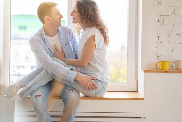 Young happy couple hugging on the windowsill in their apartment, - Foto, immagini