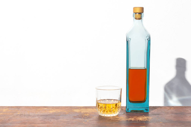 Fles en glas alcohol op oude houten tafel op witte achtergrond - Foto, afbeelding