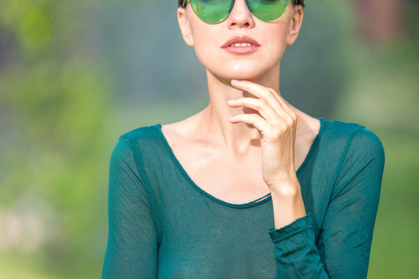 portrait of beautiful woman in green sunglasses and green dress in green natural background - Foto, imagen