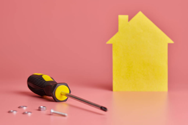Home repair and redecorated concept. House renovation. Screws and yellow house shaped figure on pink background. - Foto, afbeelding
