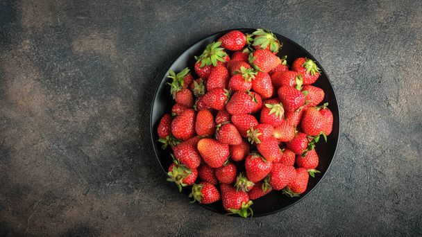 Fresh strawberries on a dark plate. On a dark background. Top view. Copy space. - Foto, immagini