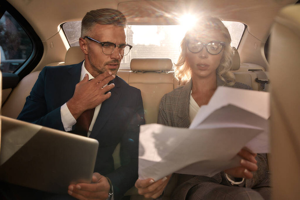 New business contract. Two business people in classic wear analyzing documents while sitting in the car - 写真・画像