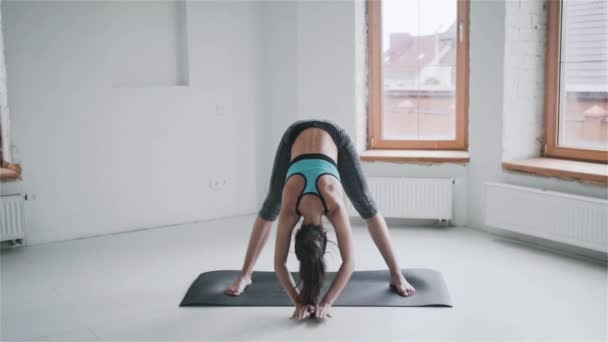 Young sporty brunette girl in sportswear does exercises in bright room at home - Materiał filmowy, wideo