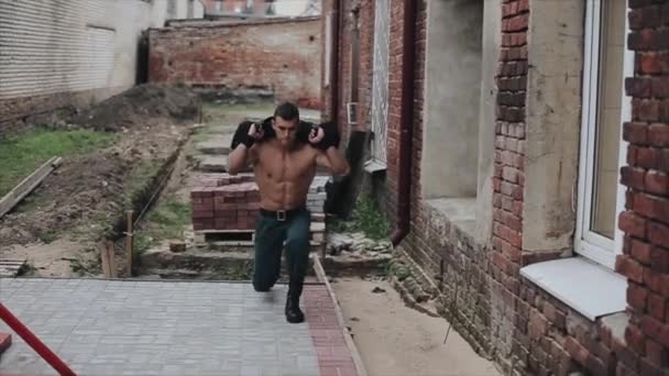 Strong handsome sportsman carrying weight on shoulders does walking lunges. Street workout - 映像、動画