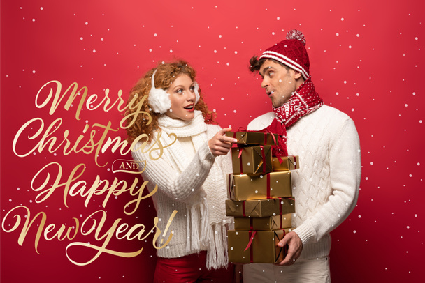 happy couple in winter outfit holding christmas presents on red with merry Christmas and happy new year lettering - Photo, Image