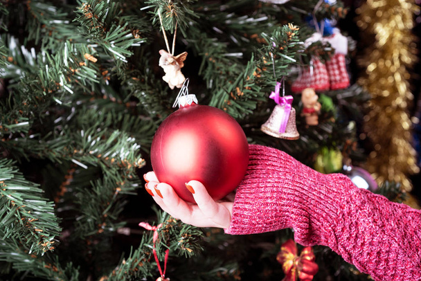 Girl decorates a Christmas tree with a red ball. - Φωτογραφία, εικόνα