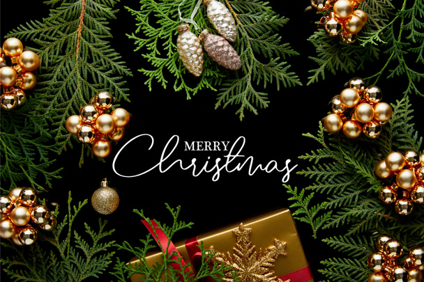 top view of shiny golden Christmas decoration, green thuja branches and gift box isolated on black with Merry Christmas illustration - Photo, Image