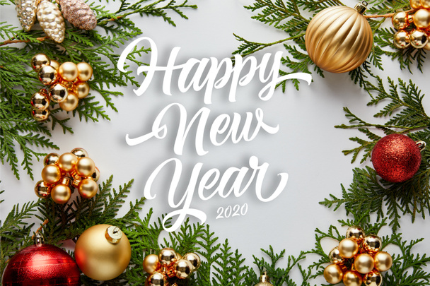 Yeşil thuja dalları üzerindeki parlak altın ve kırmızı Noel süslemeleri beyaz üzerine izole edilmiş mutlu yeni yıl harfleriyle - Fotoğraf, Görsel