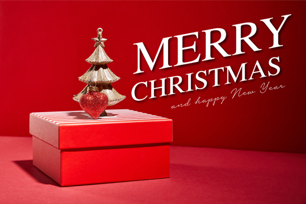 striped red gift box and decorative golden Christmas tree with bauble on red background with Merry Christmas and happy new year illustration - Photo, Image