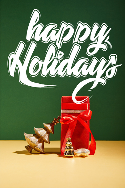 κόκκινο κουτί δώρου και διακοσμητικό χριστουγεννιάτικο δέντρο με χρυσά στολίδια σε πράσινο φόντο με λευκά γράμματα χαρούμενες διακοπές - Φωτογραφία, εικόνα