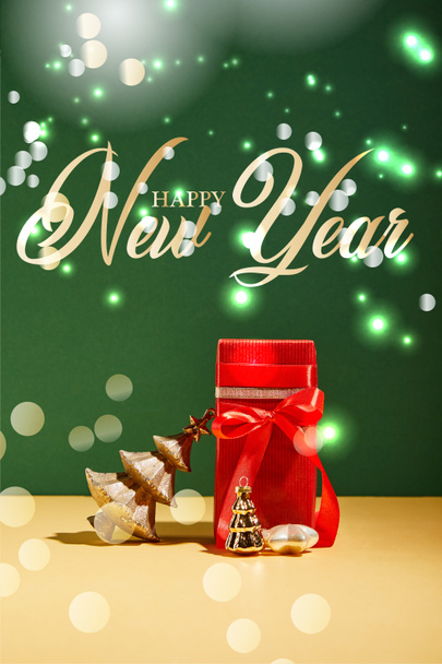 caja de regalo roja y árbol de Navidad decorativo con bolas de oro sobre fondo verde con letras feliz año nuevo
 - Foto, Imagen