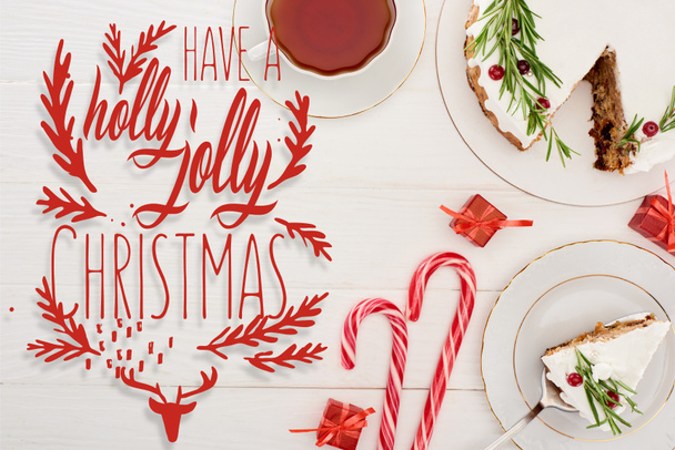 vista superior de pastel de Navidad en la mesa de madera blanca con taza de té, bastones de caramelo y pequeños regalos con tienen una letra de Navidad alegre acebo
 - Foto, Imagen
