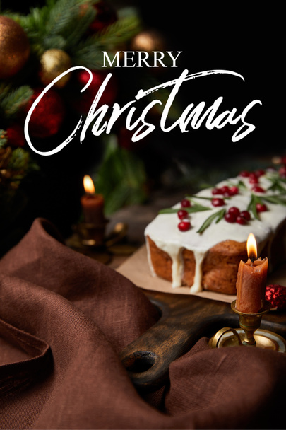 selective focus of traditional Christmas cake with cranberry near burning candles on wooden table with Merry Christmas illustration - Foto, Imagem