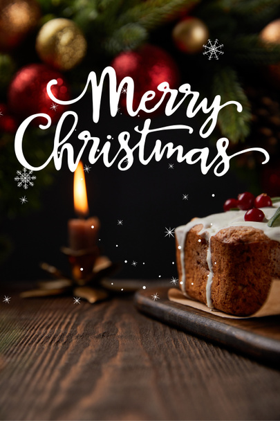 selective focus of traditional Christmas cake with cranberry near Christmas wreath with baubles and burning candle on wooden table with Merry Christmas illustration - Foto, Bild