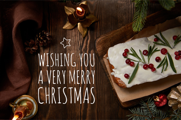 top view of traditional Christmas cake with cranberry near pine with baubles and candles on wooden table with wishing you a very Merry Christmas illustration - Photo, image