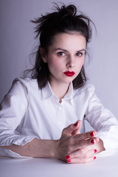 όμορφη νεαρή κοπέλα σε λευκό πουκάμισο σε λευκό φόντο με κόκκινο κραγιόν στα χείλη της - Φωτογραφία, εικόνα