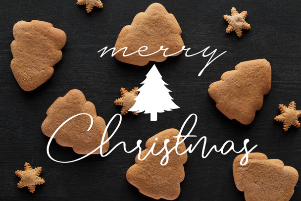 bovenaanzicht van sneeuwvlok en kerstboom koekjes op zwart houten tafel met vrolijke kerst illustratie - Foto, afbeelding
