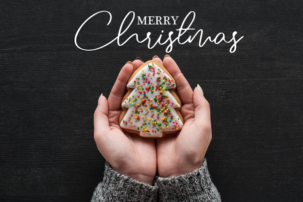 cropped view of woman holding baked Christmas tree cookie in hands with Merry Christmas illustration - Foto, Imagem
