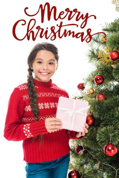 cheerful kid holding pink present near christmas tree isolated on white with merry Christmas lettering - Foto, afbeelding