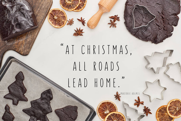 κορυφή άποψη της ακατέργαστης ζύμης για σοκολάτα Χριστουγεννιάτικα μπισκότα κοντά στα συστατικά σε λευκό φόντο με τα Χριστούγεννα όλοι οι δρόμοι οδηγούν σπίτι απόσπασμα - Φωτογραφία, εικόνα
