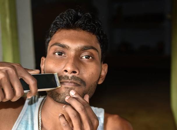 Um close-up de um jovem aparando sua barba com um aparador elétrico
. - Foto, Imagem