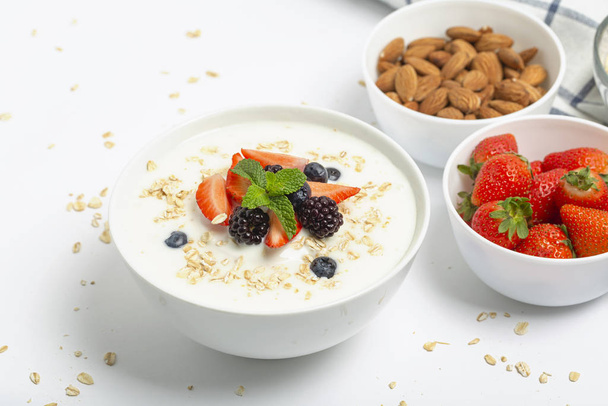 Greek yogurt with granola fresh strawberries, blueberries, blackberries and almonds on white table. Healthy snack. Breakfast food.  - Zdjęcie, obraz