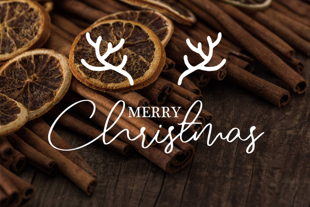 close up view of dried orange slices and cinnamon on wooden background with merry christmas illustration  - 写真・画像